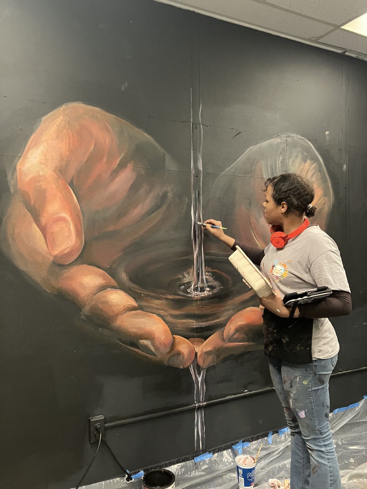 Large indoor figurative mural of hands reaching through water